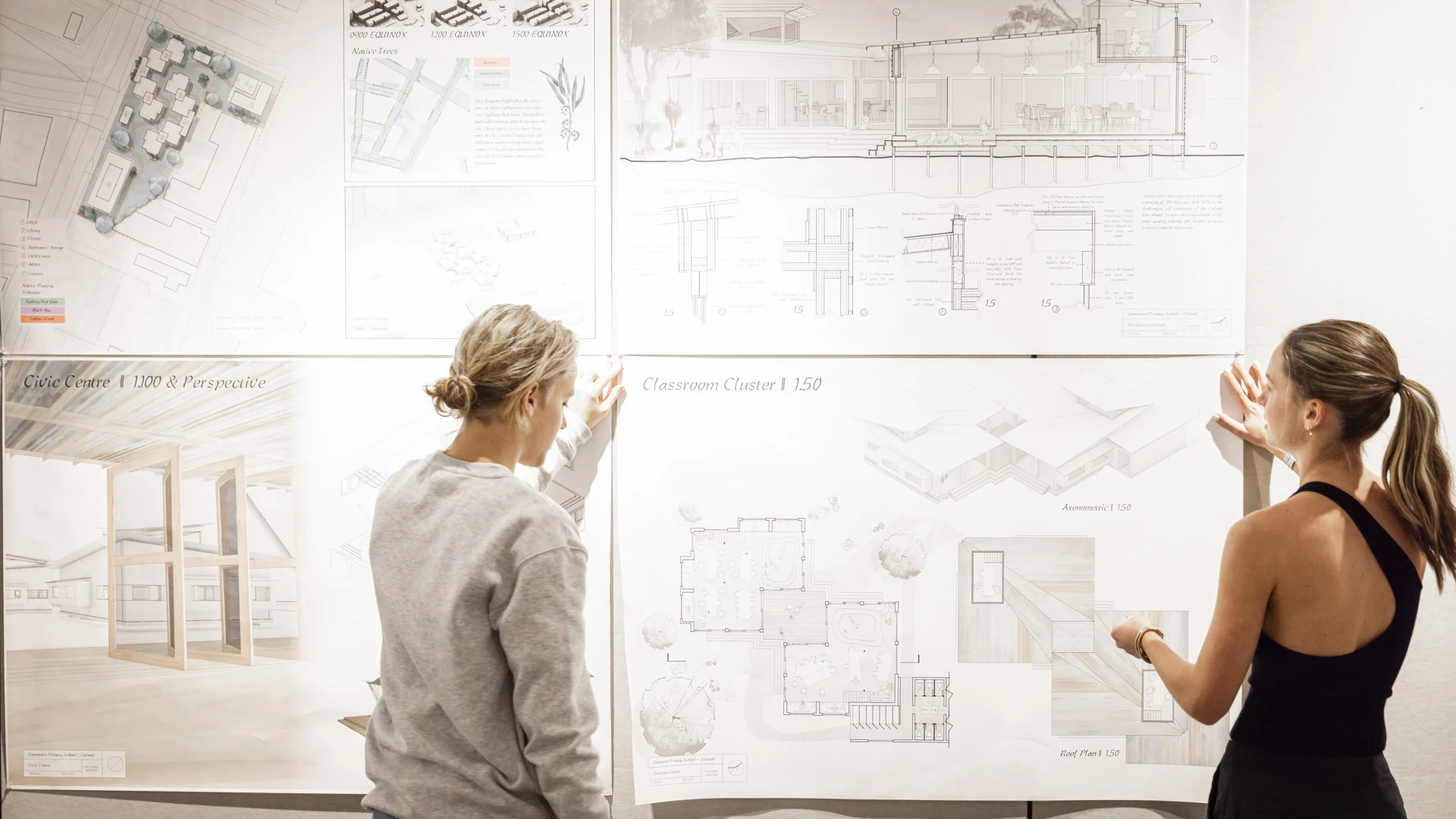 A New Zealand architectural designer reviewing large format building plans on a desk, with a modern residential house model and material samples in the background.