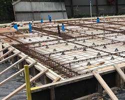 A newly poured and smoothly finished concrete slab foundation on a residential construction site in New Zealand, with steel reinforcing mesh visible at the edge.